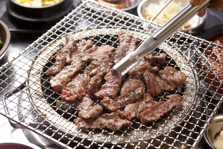 Pincers picking up soy sauce marinated beef ribs being grilled on charcoal grillの写真素材