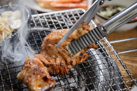 Scissors cutting pork ribs being grilled on charcoal grillの写真素材