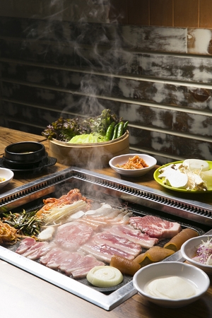 Pork belly, duck meat, pork neck, pork skin being grilled on black grillの写真素材