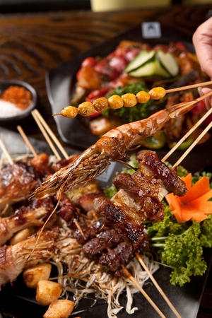 Hand picking up ginkgo nut skewers, shrimp skewer, pork belly mushroom skewer on black plateの写真素材