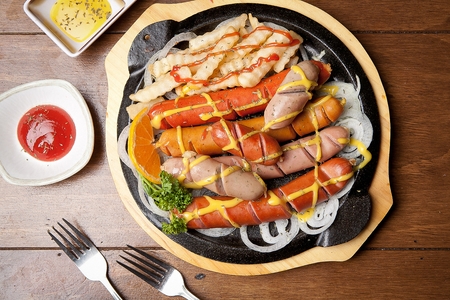 Sausages and french fries with sprinkled ketchup and mustard, on black oven plateの写真素材