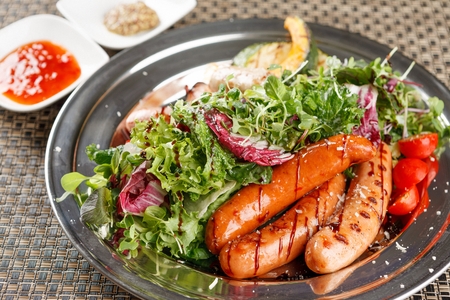 Grilled green pumpkins, sweet pumpkins, sausages and salad on silver plateの写真素材