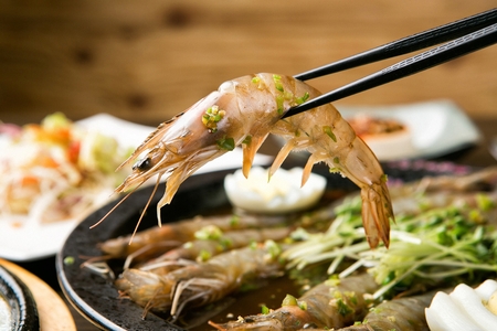 Chopsticks picking up shrimp seasoned in soy sauce, on round black plateの写真素材