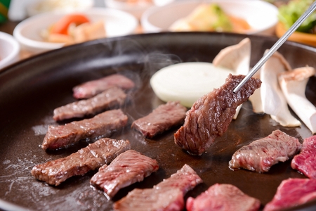 Chopsticks picking up beef thin skirt being grilled on round grillの写真素材