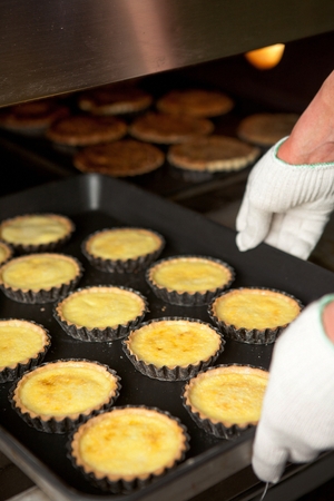 Chef's gloved hand getting freshly baked egg tarts from the ovenの写真素材