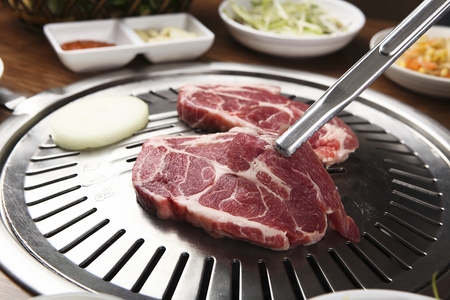 Pincers picking up beef sirloin being grilled on charcoal grillの写真素材