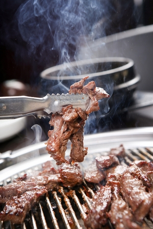 Pincers picking up pork skirt meat being grilled on charcoal grillの写真素材