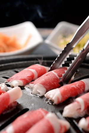 Pincers picking up beef brisket being grilled on charcoal grillの写真素材