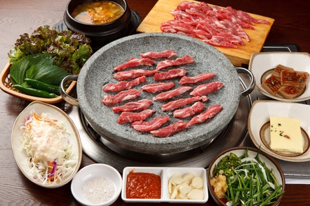 Beef rib meat being grilled on round stone plate, with vegetables, salad, acorn jelloの写真素材