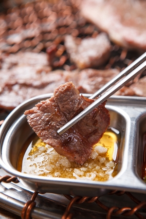 Chopsticks dipping beef sirloin being grilled on charcoal grill, in salt and sesame oilの写真素材