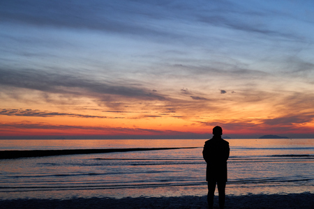Silhouette of people standing on pier with sunset above seaの写真素材