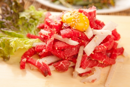 Beef tartare with sliced pear and egg yolk, on wooden cutting boardの写真素材