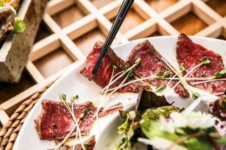 Chopsticks picking up beef tataki with microgreens from white plateの写真素材