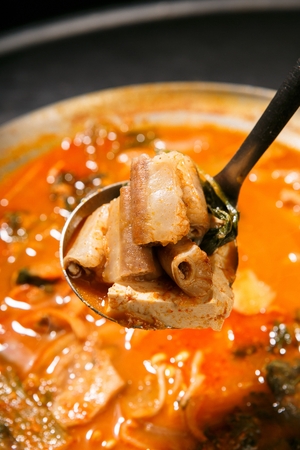 Ladle scooping up beef tripe hot pot with various vegetables such as welsh onions and onions, in pot