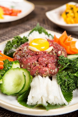 Beef tartare with sliced pear, carots and egg yolk on white plateの写真素材