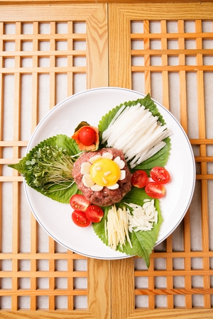 Beef tartare with cherry tomatoes, sliced pear and microgreens, on white plateの写真素材