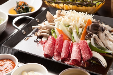 Bulgogi with carrots, welsh onions, mushrooms on rectangular iron plate, with side dishesの写真素材