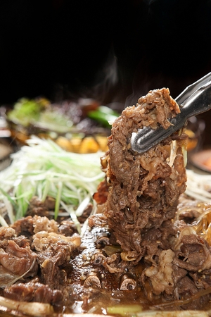 Pincers picking up marinated bulgogi with various vegetables such as welsh onions and mushrooms, in potの写真素材