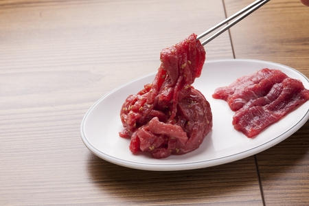 Chopsticks picking up raw meat and non-seasoned beef tartare from white plateの写真素材