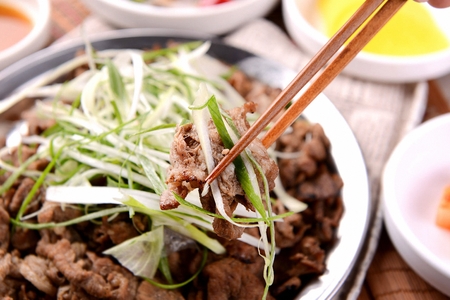 Chopsticks picking up bulgogi with seasoned green onions, on grey plateの写真素材