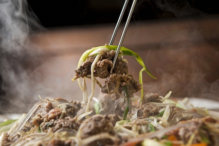 Chopsticks picking up bulgogi with marinated green onions, on plateの写真素材