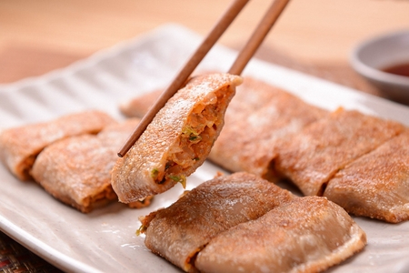 Chopsticks picking up buckwheat crepe from white rectangular plate