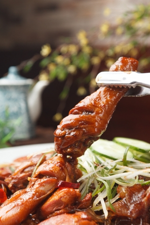 Pincers picking up meat from braised spicy chicken with carrots, welsh onions, glass noodles on white bowlの写真素材