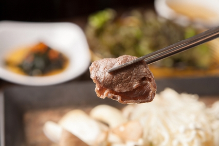 Chopsticks picking up bulgogi with carrots, welsh onions, mushrooms on rectangular iron plateの写真素材