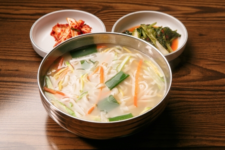 Chopped noodles soup with walsh onion and carrots in bowl, served with kimchi