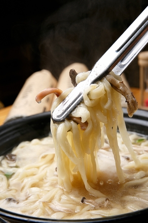 Pincers grabbing chopped noodles boiling in potの写真素材
