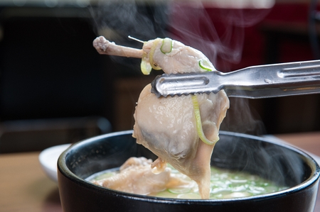 Pincers picking up the leg from chicken soup with walsh onion and ginseng, in potの写真素材