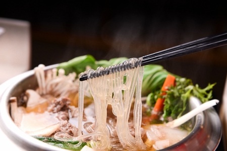 Chopsticks picking up glass noodles from shabu-shabu made of various vegetables such as mushrooms...