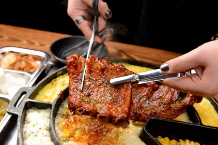 Pincers and scissors cutting grilled back ribs with cheese and egg, on iron plateの写真素材