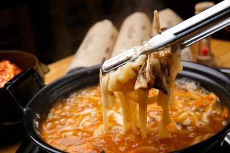 Pincers grabbing the noodles from spicy chopped noodles soup with mushrooms and crown daisy, in potの写真素材