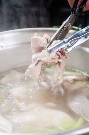 Pincers picking up the leg from chicken soup with various vegetables such as walsh onions and mushrooms, in potの写真素材