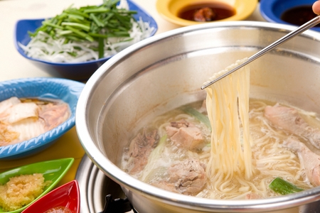Chopsticks grabbing chopped noodles soup with vegetables boiling in potの写真素材