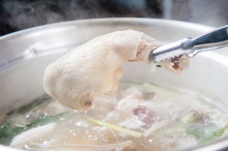 Pincers picking up the leg from chicken soup with various vegetables such as walsh onions and mushrooms, in potの写真素材
