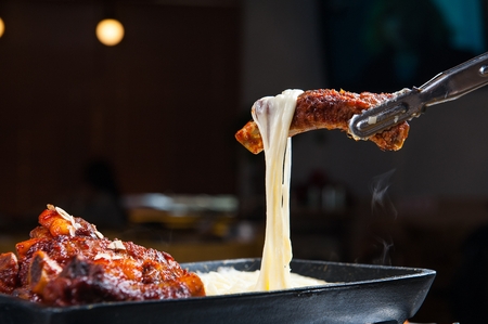 Pincers picking up grilled back ribs with cheese on iron plateの写真素材