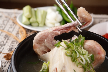 Chopsticks picking the leg from chicken soup with walsh onion and ginseng, in potの写真素材