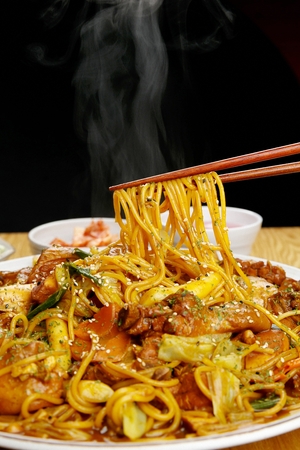 Chopsticks picking up curry-chicken stir-fried noodles, including carrots, cabbage and chicken meat, on white plateの写真素材