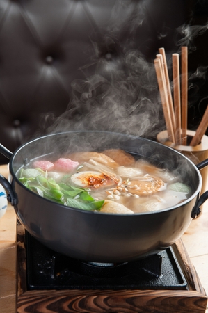 Hot fish cake soup with various vegetables such as crown daisy, on pot on mini burnerの写真素材