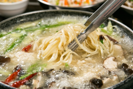 Pincers picking up chopped noodles from duck shabu-shabu broth with various vegetables such as mushrooms and chives, in potの写真素材