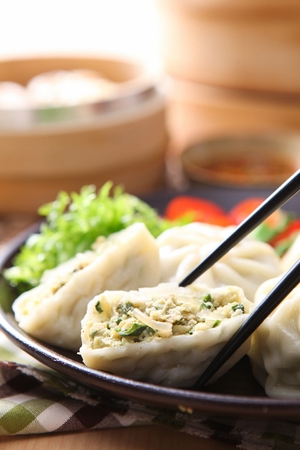 Chopsticks grabbing steamed dumplings from black plateの写真素材