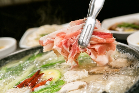 Pincers dipping duck meat in duck shabu-shabu broth with various vegetables such as mushrooms and chives, in potの写真素材