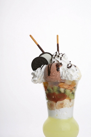 Fruit frappe with whipping cream, chocolate ice cream and snacks on top, in plastic cupの写真素材