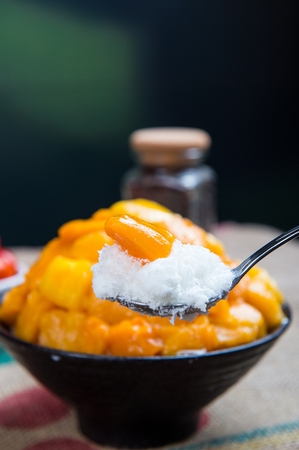 Spoon scooping up mango shaved ice with mangoes, in white bowlの写真素材