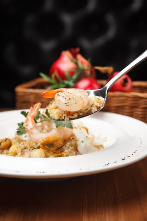 Spoon scooping up stir-fried rice with mussels and shrimp on white plateの写真素材