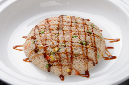 Stir-fried rice with peas, corn and carrots with sprinkled sauce, on white plateの写真素材