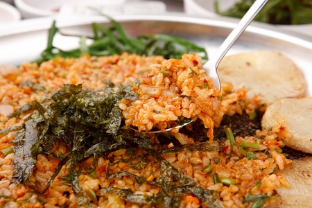 Spoon scooping up stir-fried kimchi rice with sprinkled dried seaweed on plateの写真素材