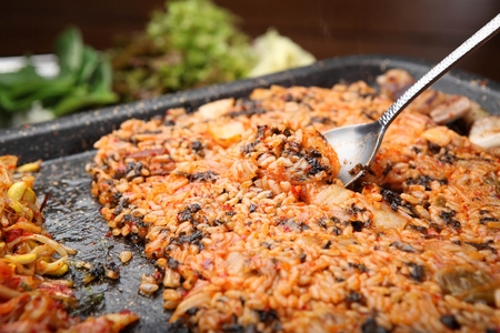 Spoon scooping up stir-fried rice with carrots, walsh onions and dried seaweed powder, made on iron plateの写真素材